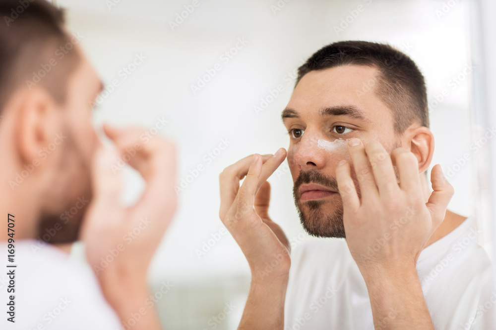 young man applying cream to face at bathroom young man applying cream to face at bathroom