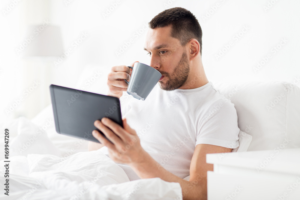 man with tablet pc drinking coffee in bed at home man with tablet pc drinking coffee in bed at home