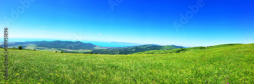 Panorama summer flower meadow in the mountains  tourism. Beautiful sea view landscape. Fresh green rural meadows on a sunny day with blue sky. Scenery view ocean