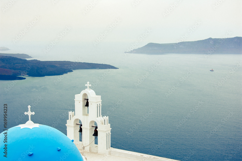 Bell tower of an orthodox church at Santorini with volcano at the background, Greece.