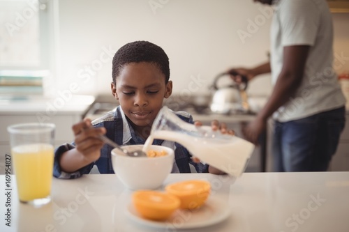 Boy pouring milk into breakfast cereals bowl in kitchen
