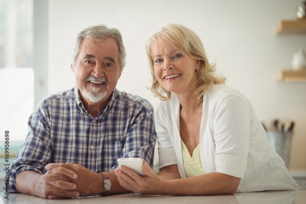 Senior couple using mobile phone in the kitchen Senior couple using mobile phone in the kitchen
