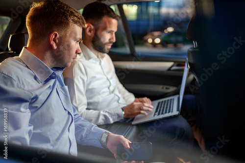 Businesspeople work on late night in back seat of car.