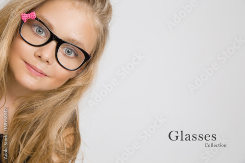 Portrait of a lovely little girl daughter in long blond hair and black glasses with pink bow which looks at the camera, photo on the white background ammazing eyes photo