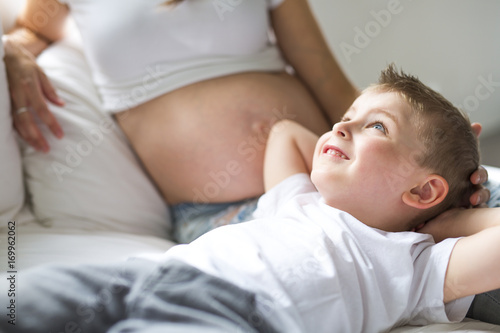 Beautiful pregnant young mother, sitting in bed with her older child