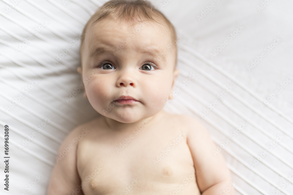 Cute happy 7 month baby girl in diaper lying and playing