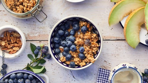 Granola with natural yogurt, fresh blueberries, nuts and honey, delicious breakfast or dessert, top view. Healthy eating concept. Stop motion animation.