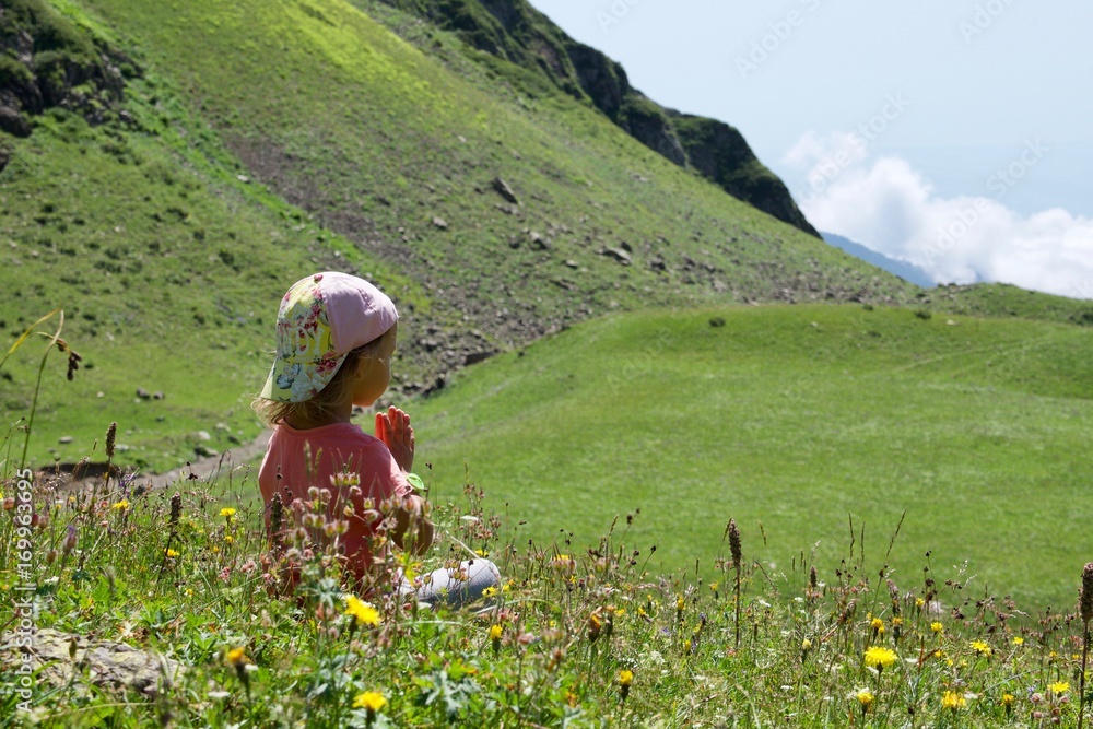 Little cute girl meditating in mountain landscape.
