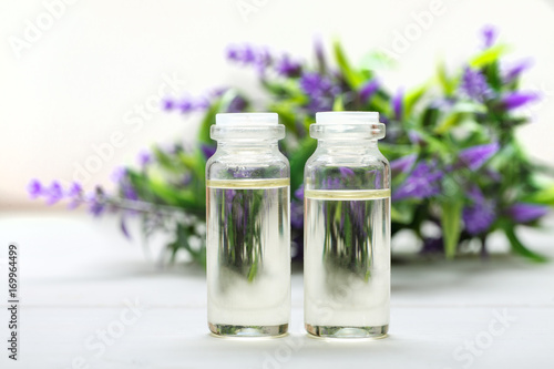 Two glass bottles with oil in it and lavender flower on the background on a white wooden table