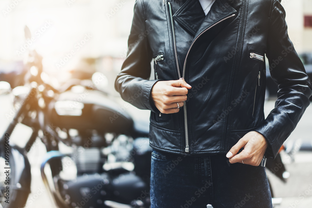Obraz premium Girl unfastens black leather jacket on background motorcycle in sun flare city, hipster biker female hands closeup, motorbike street lifestyle, traveler planing bike route in summer holiday concept