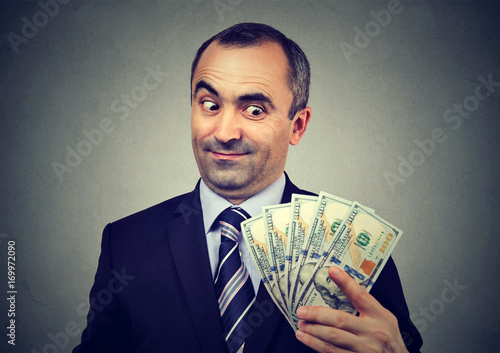 Obraz na plátne Funny sly business man holding looking at money dollar banknotes