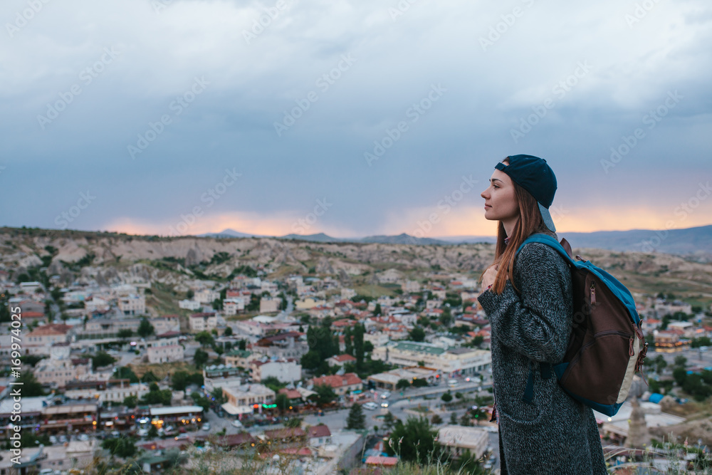 Young woman tourist stands on a sunset background over the city of Goreme in Turkey. Cappadocia. Tourism, rest, vacation.