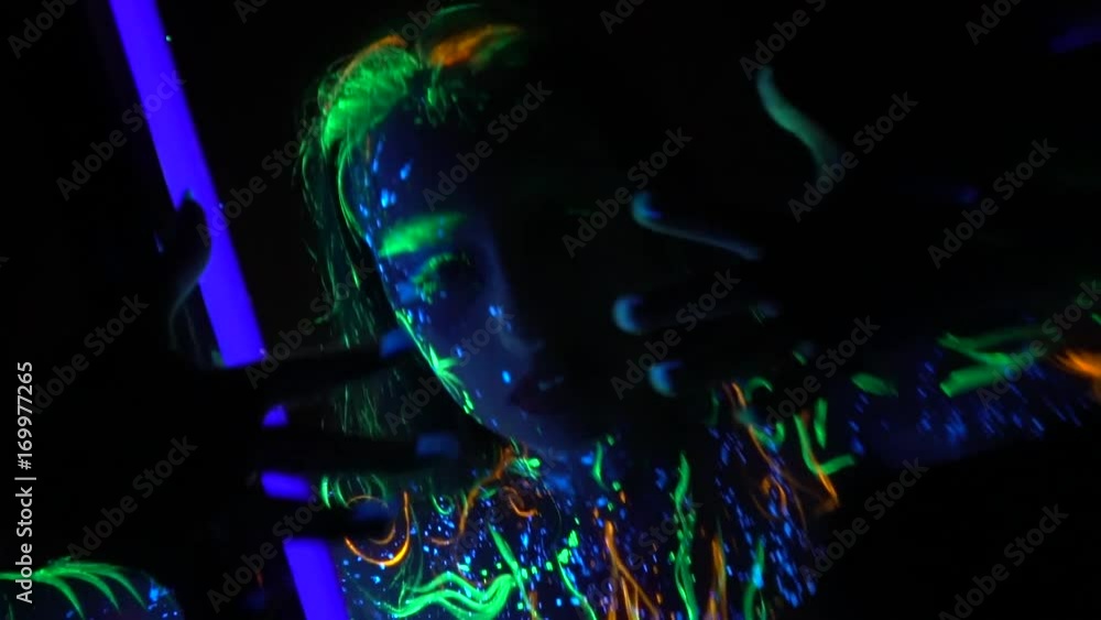 A beautiful girl in patterns gently dances near a fluorescent lamp in the dark A beautiful girl in patterns gently dances near a fluorescent lamp in the dark