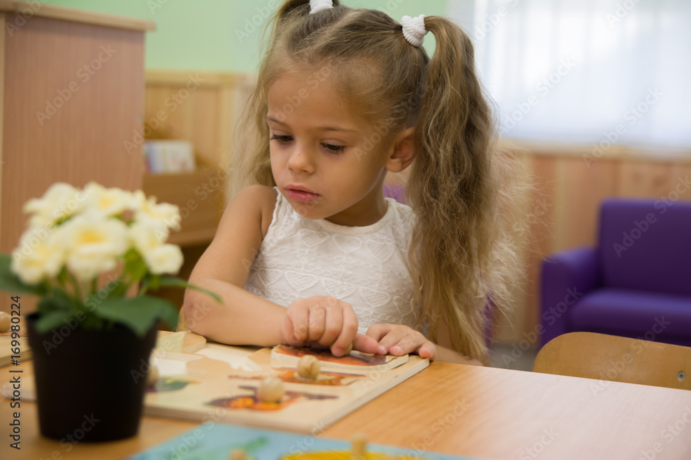 Happy little child, adorable blonde toddler girl, having fun playing with jigsaw puzzle assembling pieces of picture together sitting indoors at small white table Happy little child, adorable blonde toddler girl, having fun playing with jigsaw puzzle assembling pieces of picture together sitting indoors at small white table
