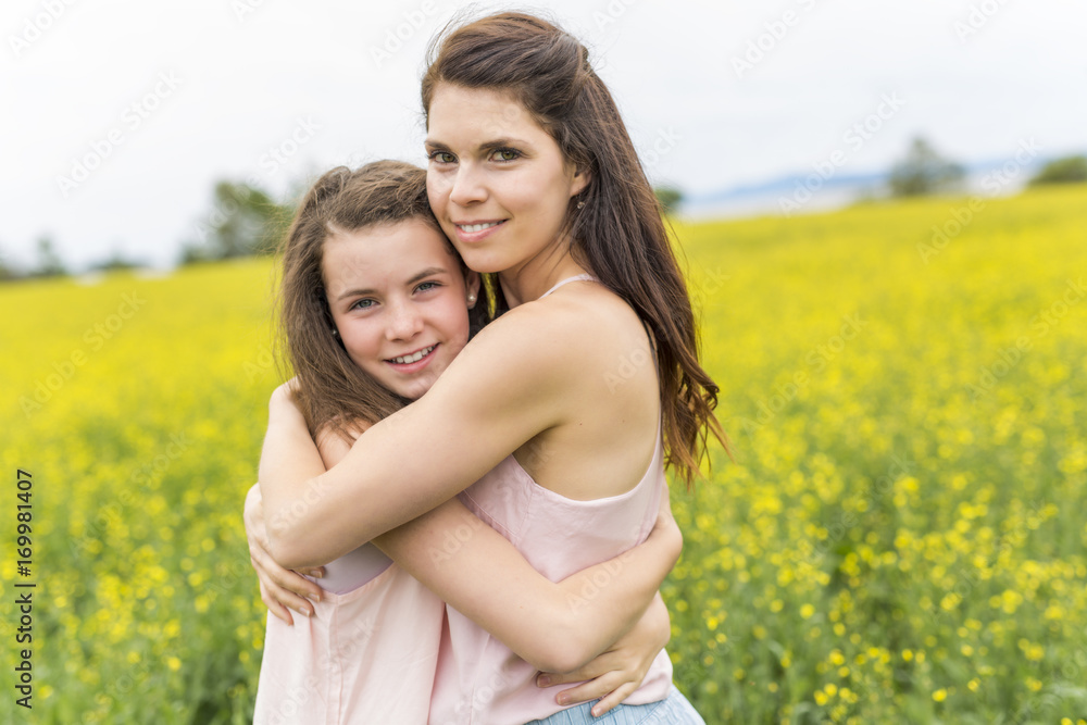 Happy family mother and child daughter embrace on yellow flowers on nature in summer Happy family mother and child daughter embrace on yellow flowers on nature in summer
