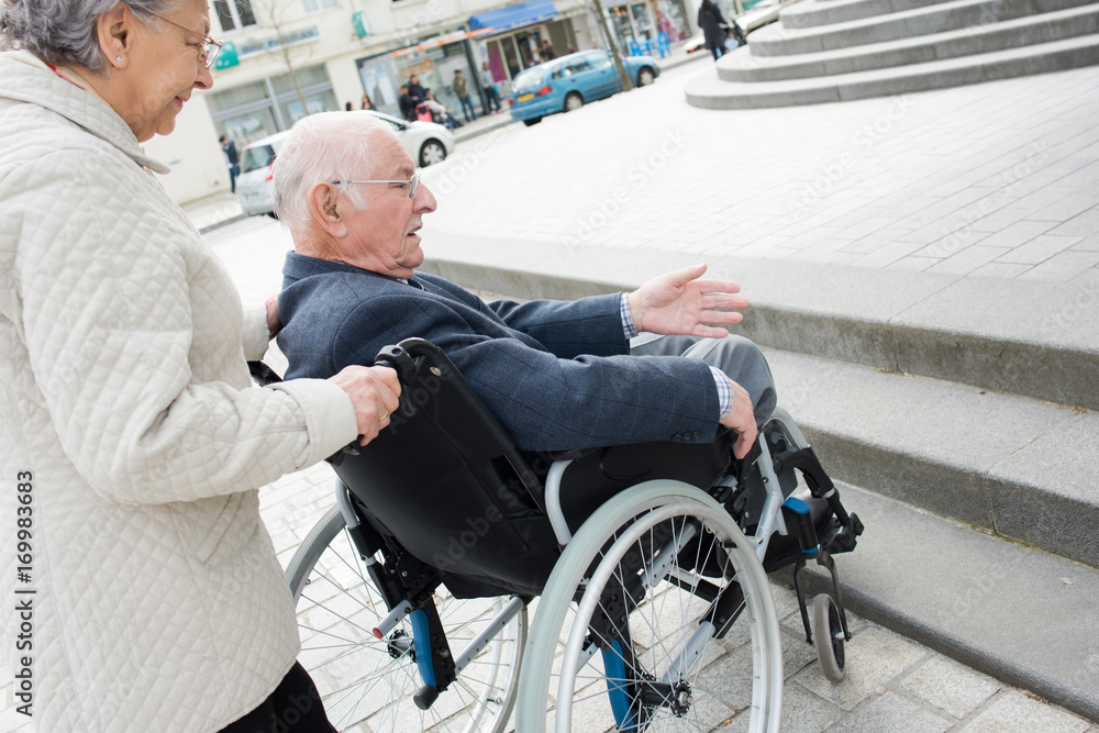 Obraz premium senior couple having trouble moving disabled husband through the city
