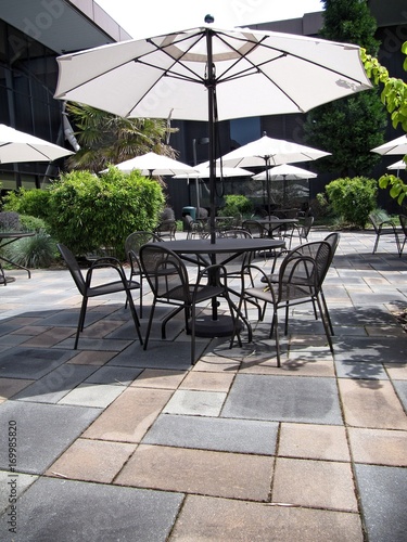   Patio with black metal tables and chairs and white umbrellas.
