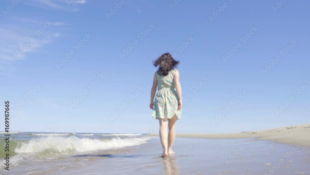 Attractive young woman in a dress strolls along the seacoast barefoot and enjoys herself. Beach with white sand. Outgoing coastal line. Slow Motion. Attractive young woman in a dress strolls along the seacoast barefoot and enjoys herself. Beach with white sand. Outgoing coastal line. Slow Motion.