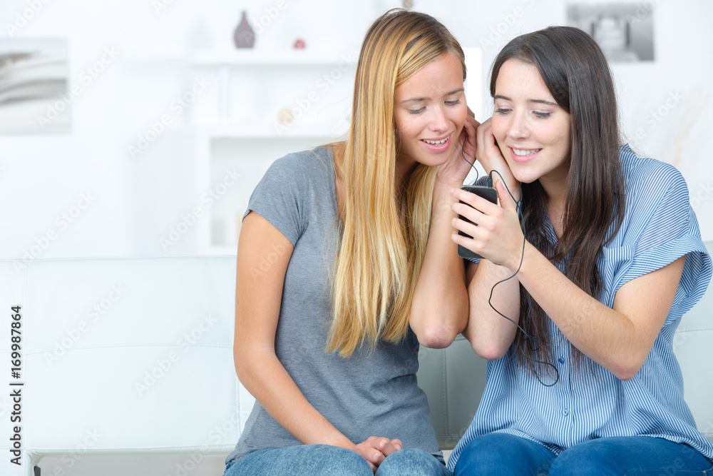 Friends sharing headphones connected to a cellphone Friends sharing headphones connected to a cellphone
