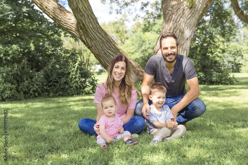 Parents Sitting With Children In Field close to a tree