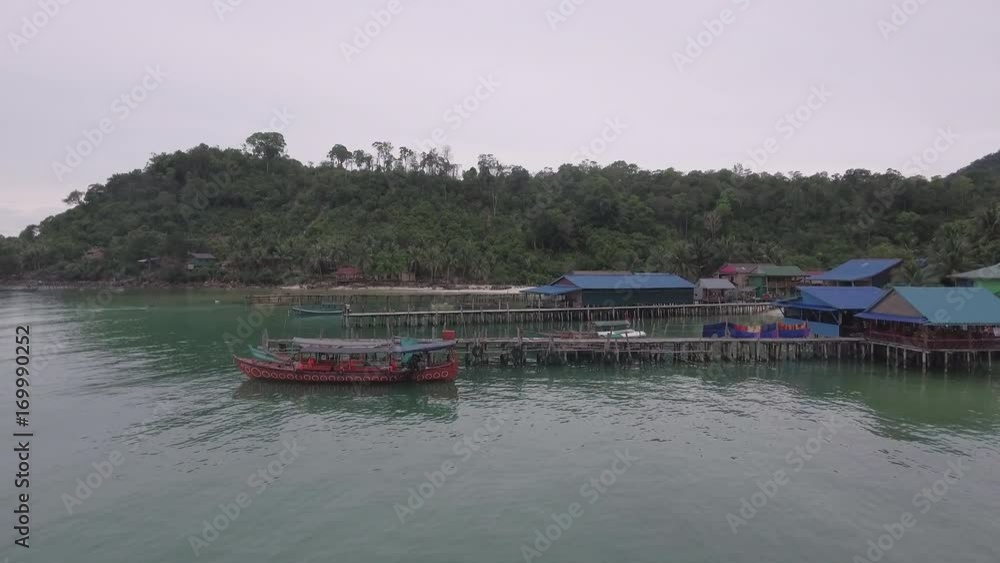 drone view: flying over fishing boats docked at wooden piers and a fishing village. A fisherman fishing a pole one of the piers. drone view: flying over fishing boats docked at wooden piers and a fishing village. A fisherman fishing a pole one of the piers.