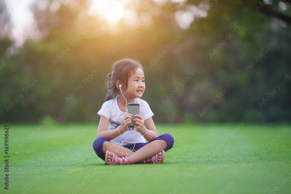 Children, technology and leisure concept - girl with headphones lying on natual and listening to music Children, technology and leisure concept - girl with headphones lying on natual and listening to music