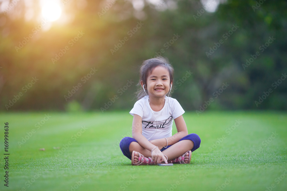 Children, technology and leisure concept - girl with headphones lying on natual and listening to music Children, technology and leisure concept - girl with headphones lying on natual and listening to music