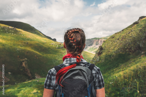 Unrecognizable traveler woman with backpack enjoying view of summer mountains, rear view