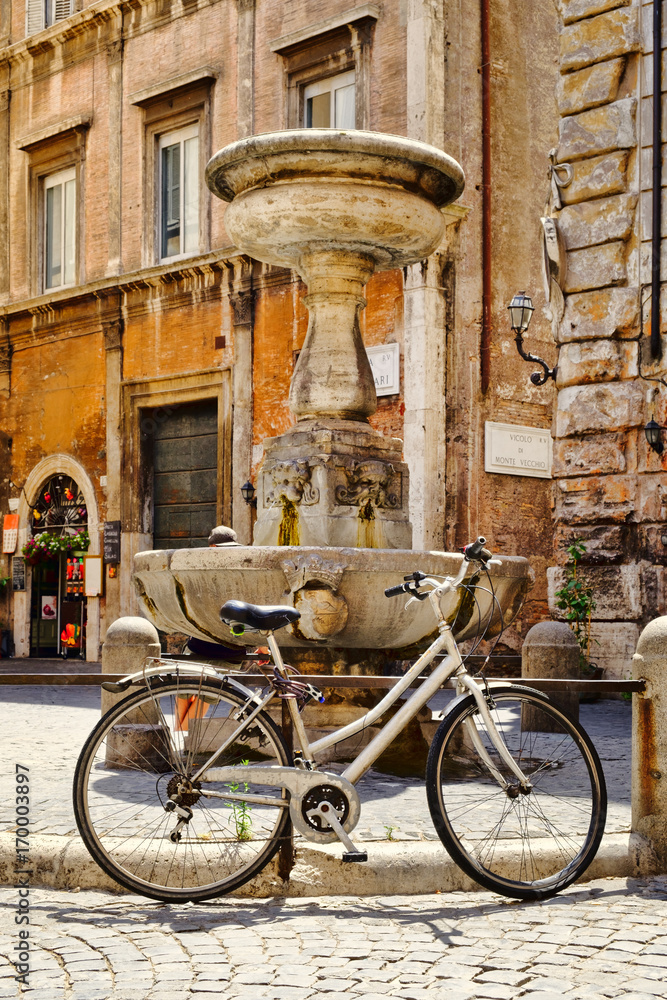 Fototapeta premium Old bicycle next to a fountain at a small square in central Rome
