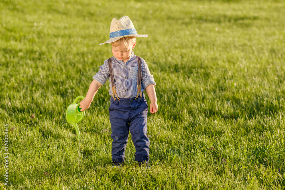 Toddler child outdoors. One year old baby boy wearing straw hat using watering can Toddler child outdoors. One year old baby boy wearing straw hat using watering can