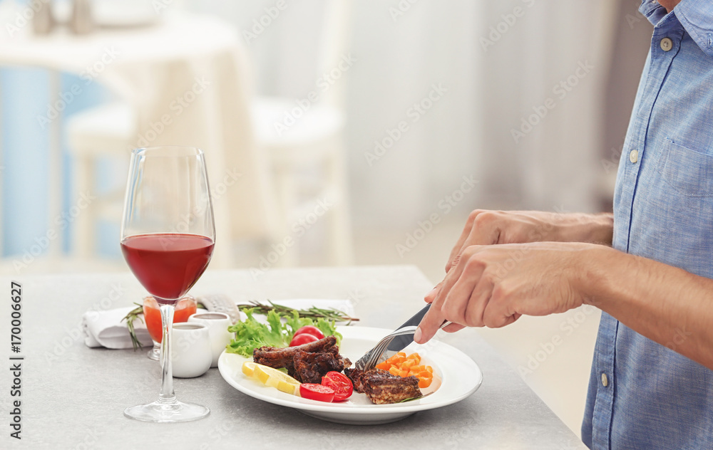 Young man eating delicious roasted ribs in restaurant