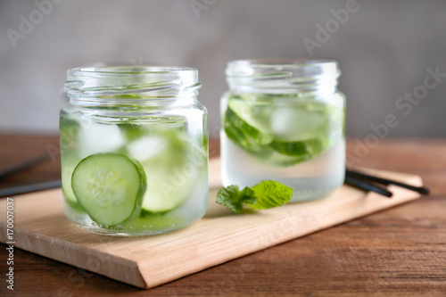 Delicious refreshing water with mint and cucumber in glass jars on wooden table