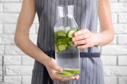 Young woman holding bottle of delicious refreshing water with mint and cucumber, closeup