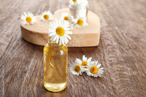 Bottle of essential oil and chamomile flowers on table