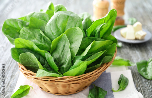 Wicker basket with fresh spinach leaves on table