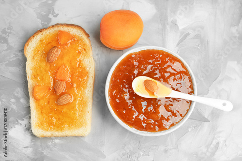 Slice of bread and bowl with apricot jam on gray textured background