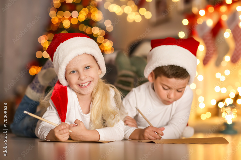 Cute kids writing letter to Santa in room decorated for Christmas Cute kids writing letter to Santa in room decorated for Christmas