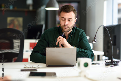 Young man studying with laptop computer on white desk.