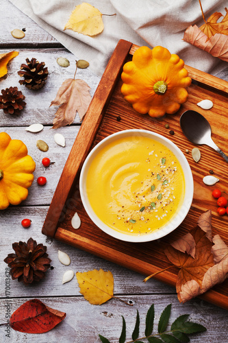 Vintage tray with warm autumn pumpkin soup decorated seeds and thyme in white bowl on rustic wooden table top view. Llifestyle shot for halloween menu.