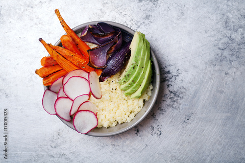 Fresh healthy vegetarian bowl for lunch with baked carrots and red onion, coucous and sliced avocado. Simple and colourful organic food concept. Minimalistic flat lay with copy space. photo