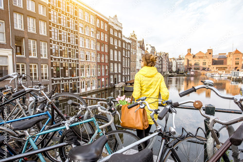 Obraz premium Young woman in yellow raincoat enjoying morning view on the beautiful cityscape view in Amsterdam