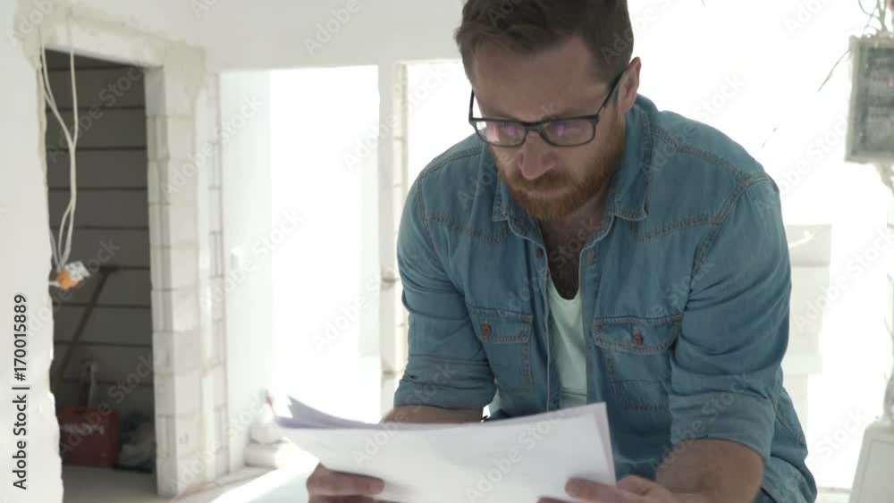 Young man checking project on papers sitting on ladder at his new apartment
Young man checking project on papers sitting on ladder at his new apartment