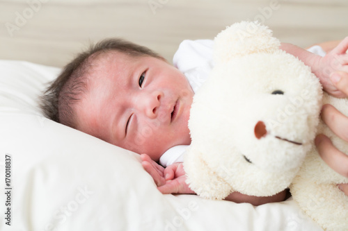 Hug teddy and sleeping newborn baby boy on a bed, 14 days of life, sleep asian kid concept