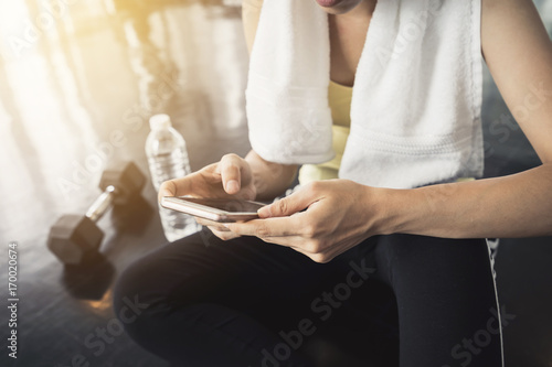 asian sportswoman with white towel using smartphone