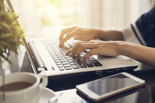 woman's hands typing on a laptop keyboard with cup of coffee