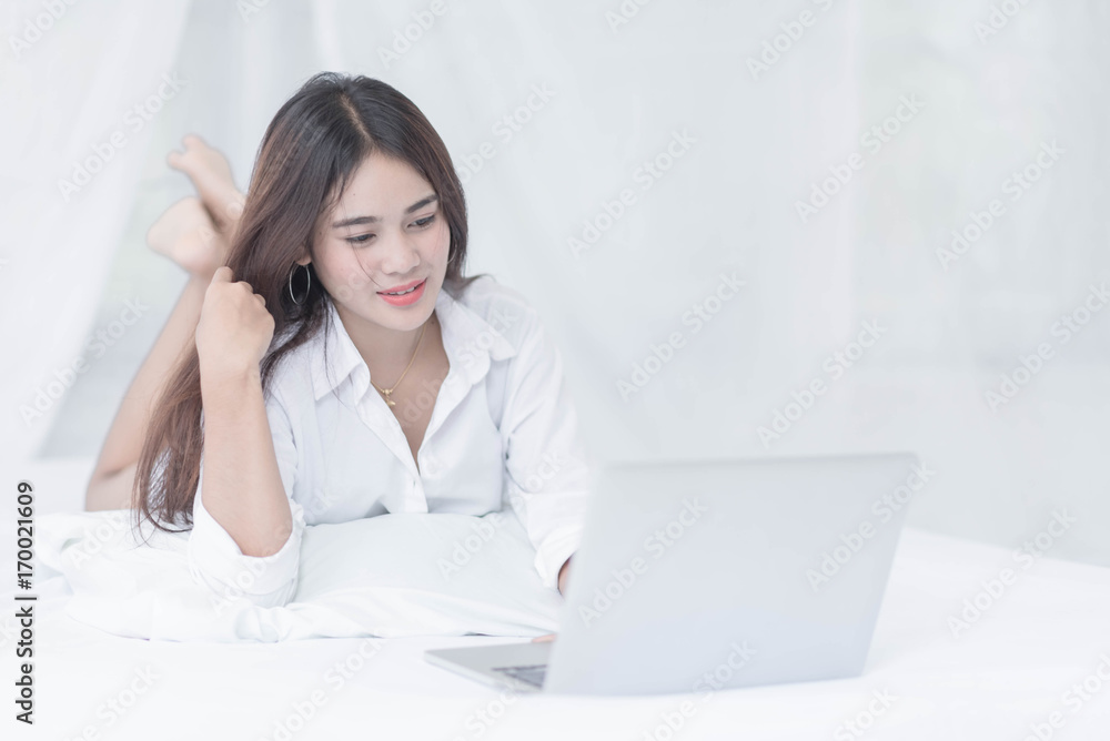 Young woman writing on a computer while in bed Young woman writing on a computer while in bed