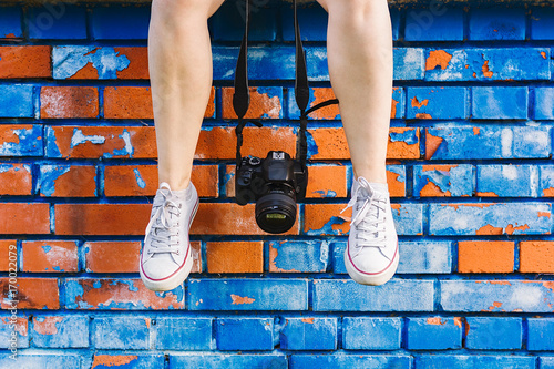 Canvastavla Woman's feet and photo camera dangling in front of blue and orange brick wall