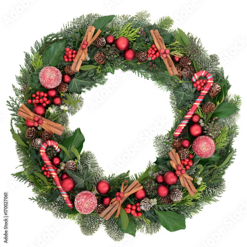 Decorative christmas wreath with bauble decorations, candy canes, cinnamon sticks, frosted apples, holly, mistletoe, ivy, snow covered  winter greenery on white background. photo