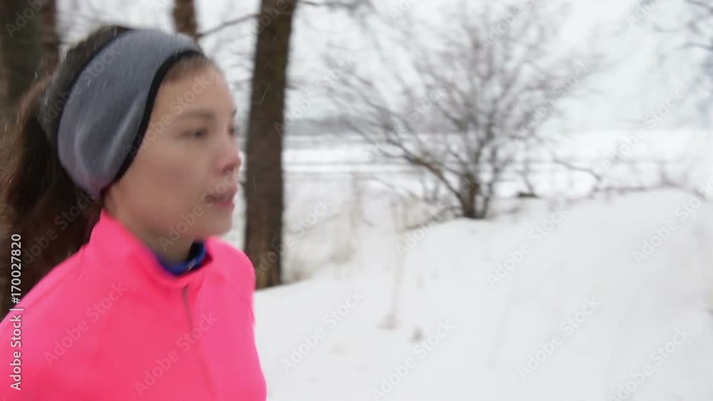 Woman jogging in snowy city park - winter fitness. Female athlete exercising outside in cold weather on forest path wearing activewear. Windbreaker pink jacket, warm tights, running shoes. Woman jogging in snowy city park - winter fitness. Female athlete exercising outside in cold weather on forest path wearing activewear. Windbreaker pink jacket, warm tights, running shoes.