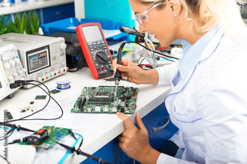 Fotografi Young female electronic engineer soldering computer motherboard in laboratory